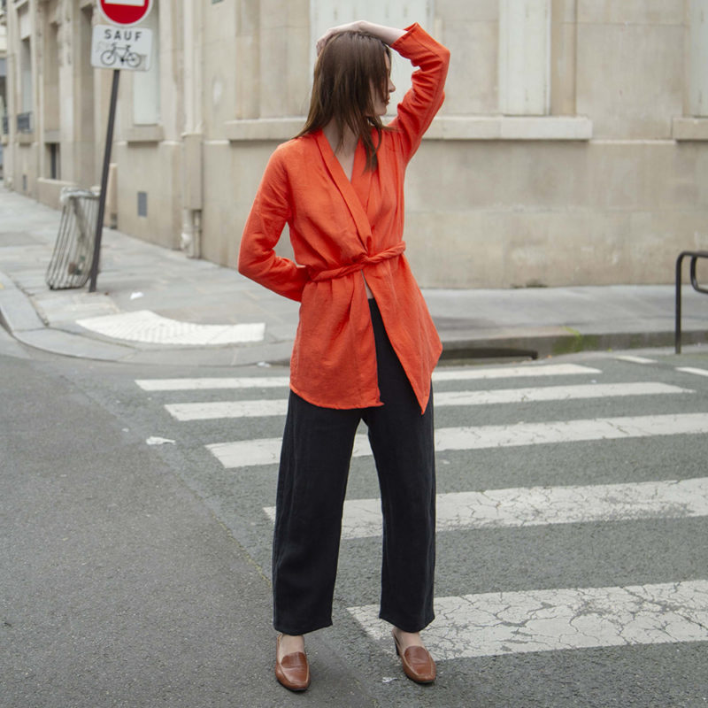 woman in bright poppy wrap blazer, black pants, brown slides standing on street