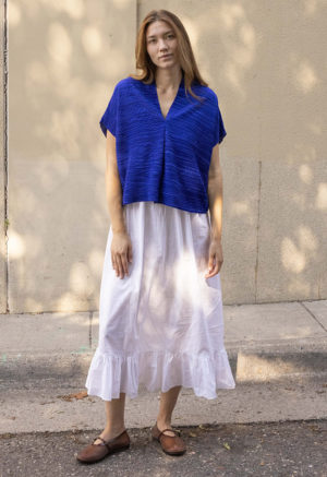 woman in cobalt blue v-neck top over white cotton skirt