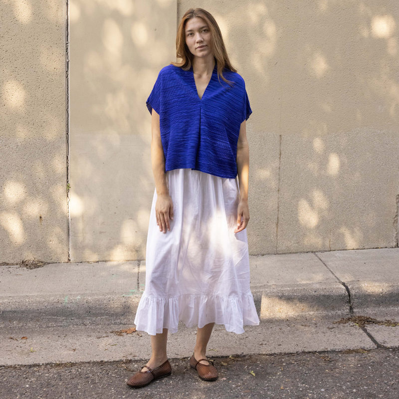 woman in cobalt blue v-neck top over white cotton skirt