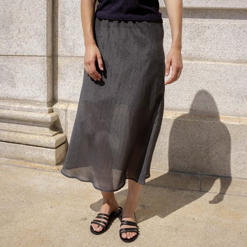 woman wearing sheer dark hazy green slip skirt, black tube top and black sandals.