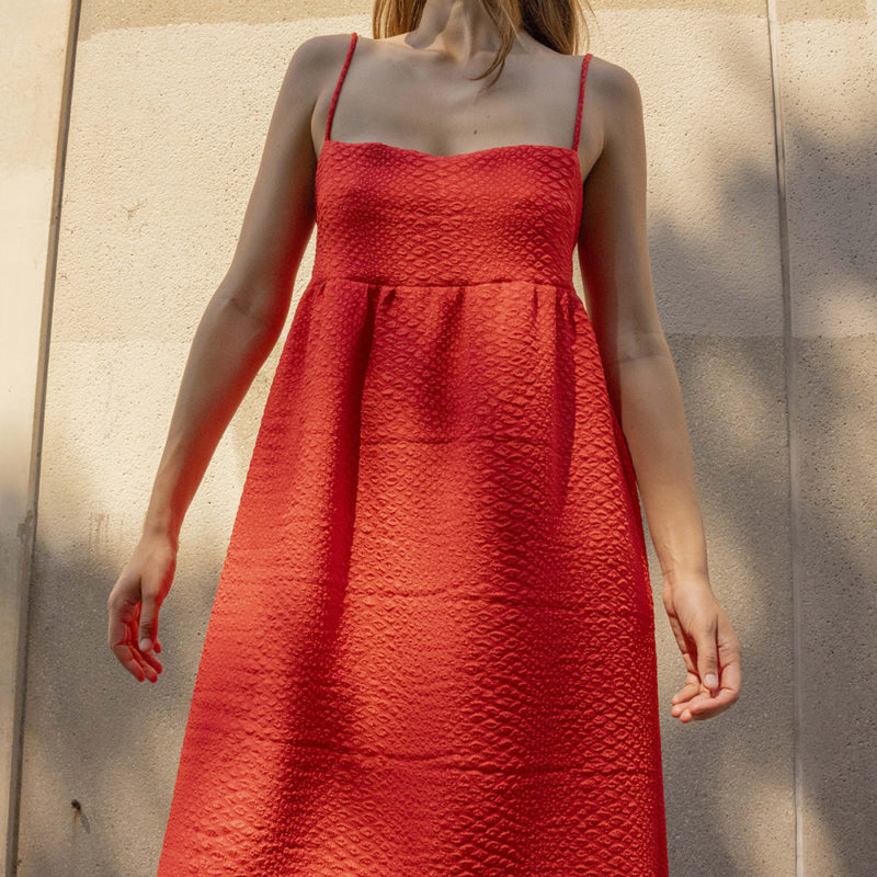 woman in bright red sundress standing in speckled sunlight