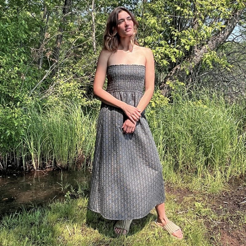 woman in dark grey charcoal strapless maxi dress standing in front of green grasses and trees