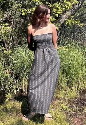 woman in dark grey charcoal strapless maxi dress standing in front of green grasses and trees