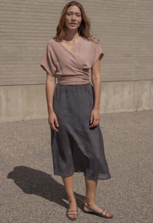 woman in blush short sleeve wrap top, dark green slip skirt and green sandals.