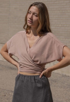 woman in blush short sleeve wrap top, dark green slip skirt and green sandals.