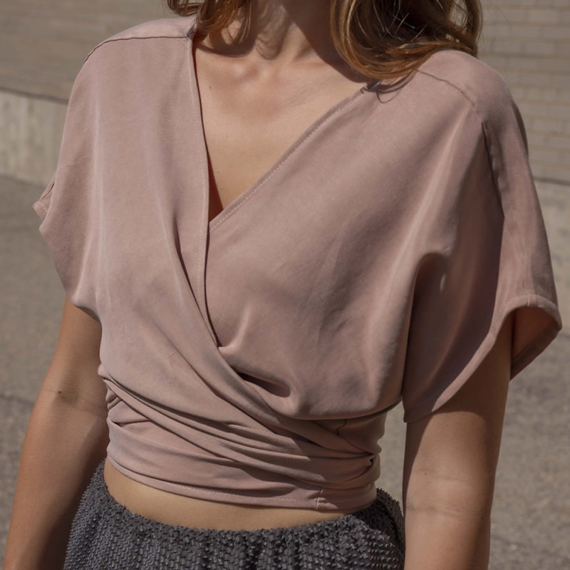woman in blush short sleeve wrap top, dark green slip skirt and green sandals.