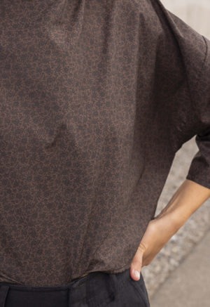 woman in dark brown and black floral boatneck top and black trousers
