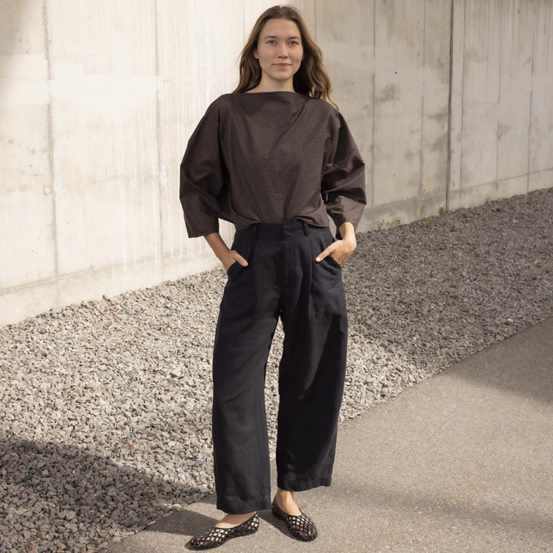 woman in dark brown and black floral boatneck top and black trousers