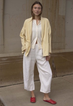 woman in cream pants, cream sweater, pale yellow jacket and red shoes