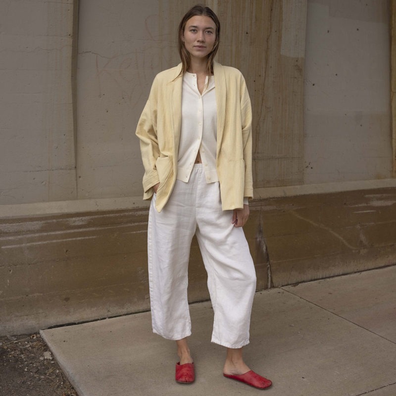 woman in cream pants, cream sweater, pale yellow jacket and red shoes