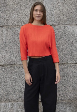 woman in bright red cropped dolman sleeve top and black trousers