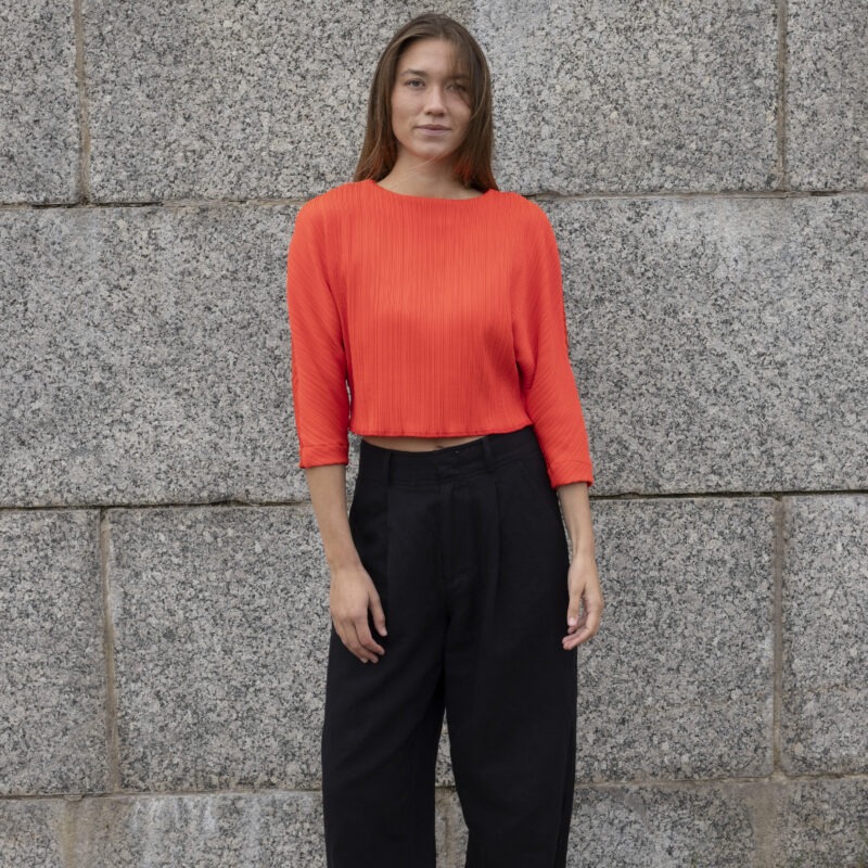 woman in bright red cropped dolman sleeve top and black trousers
