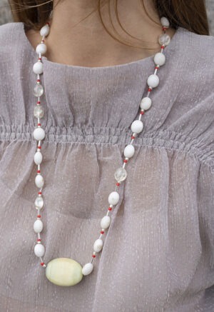 woman in grey shirt and extra long white, red and rock necklace