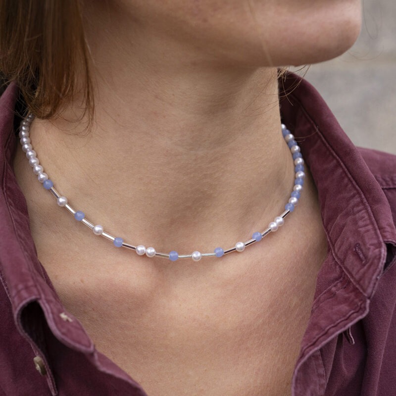 woman in maroon button-up and light blue and pearl necklace