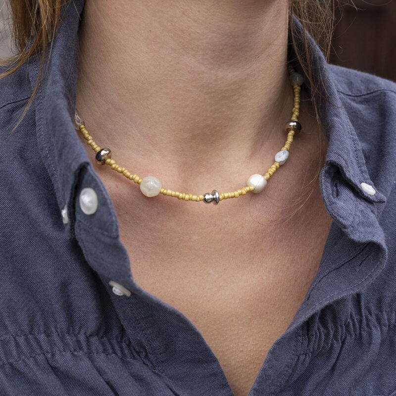 woman in dark grey button-up with yellow beaded necklace