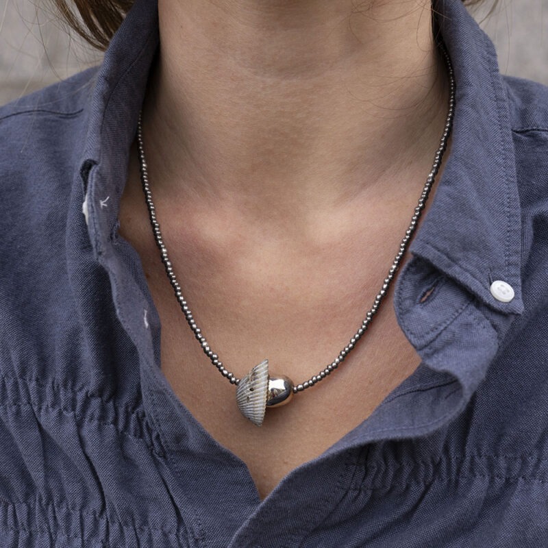 woman in grey button-up with grey and silver shell necklace