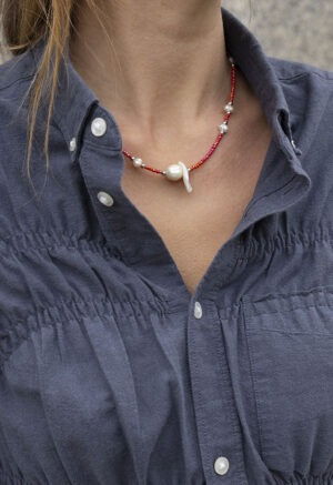 woman in dark grey button-up with red and pearl necklace