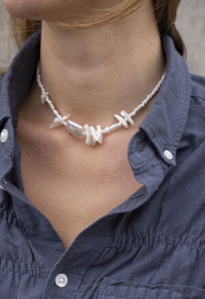 Woman in grey button-up with pearl and shell necklace