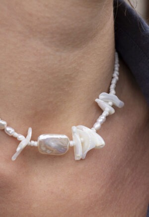 Woman in grey button-up with pearl and shell necklace