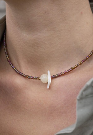 woman in grey shirt with brown and white shell necklace