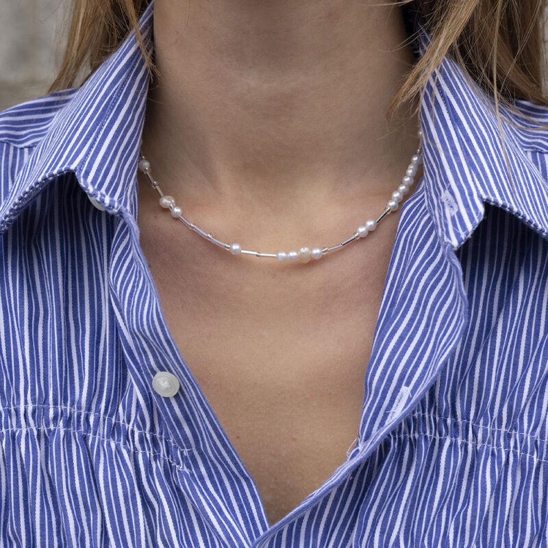 woman in blue and white strip button-up with glass and pearl beaded necklace