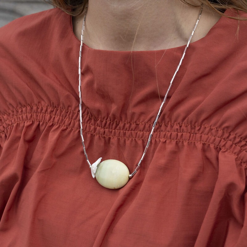 woman in burnt orange top and long silver and rock necklace.