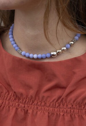 woman in burnt orange top and blue and silver beaded necklace.