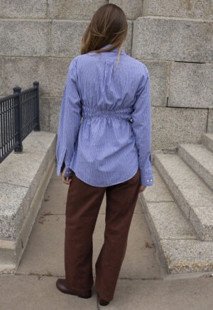 woman in blue and white stripe button-up and brown pants