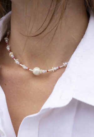woman in white button-up with pearl, red and silver necklace