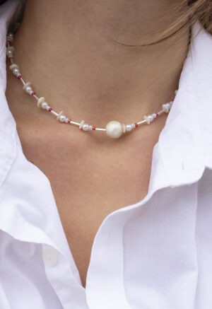 woman in white button-up with pearl, red and silver necklace