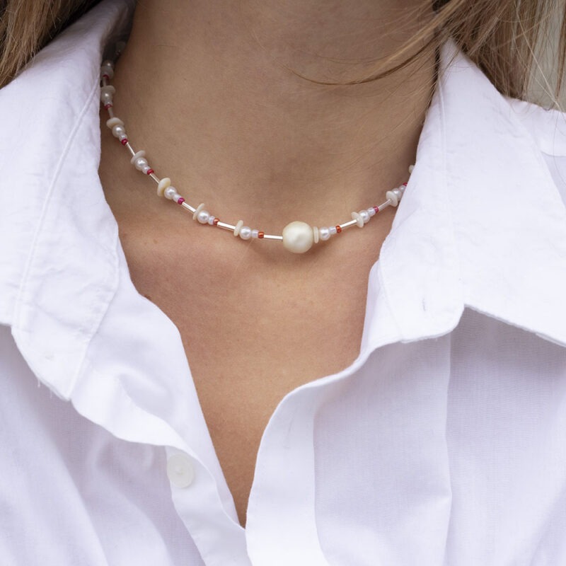 woman in white button-up with pearl, red and silver necklace